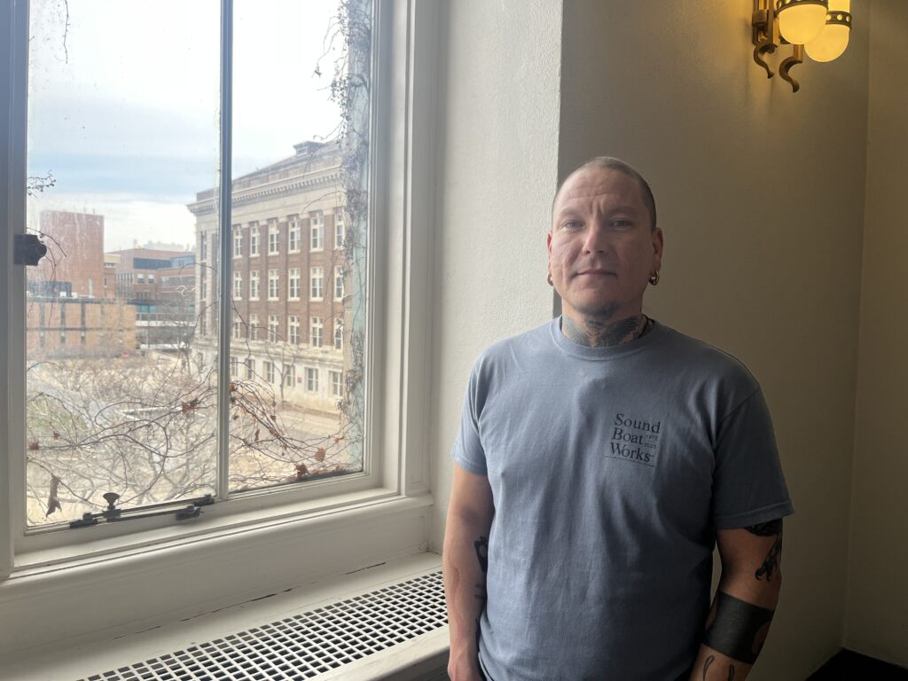 Mskwaankwad Rice, an Indigenous graduate student at the University of Minnesota, stands in front of a window in Cyrus Northrop Memorial Auditorium in Minneapolis, Minn., on Thursday, March 14, 2024. Rice is studying Anishinaabemowin in the university’s linguistics department and is currently working on his PhD dissertation.